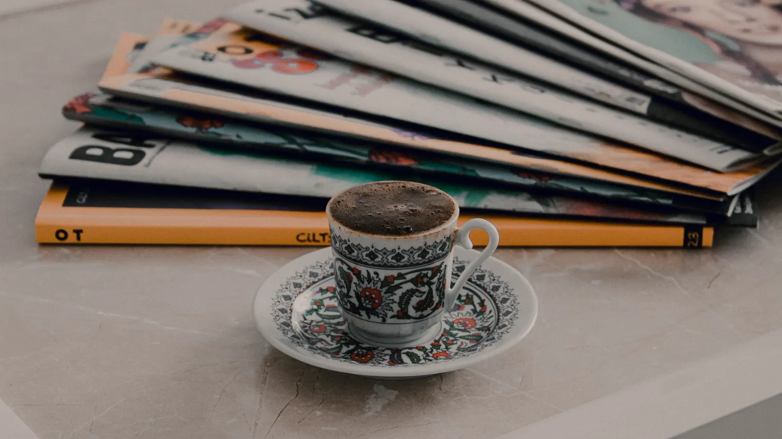 A stack of magazines beside a patterned coffee cup