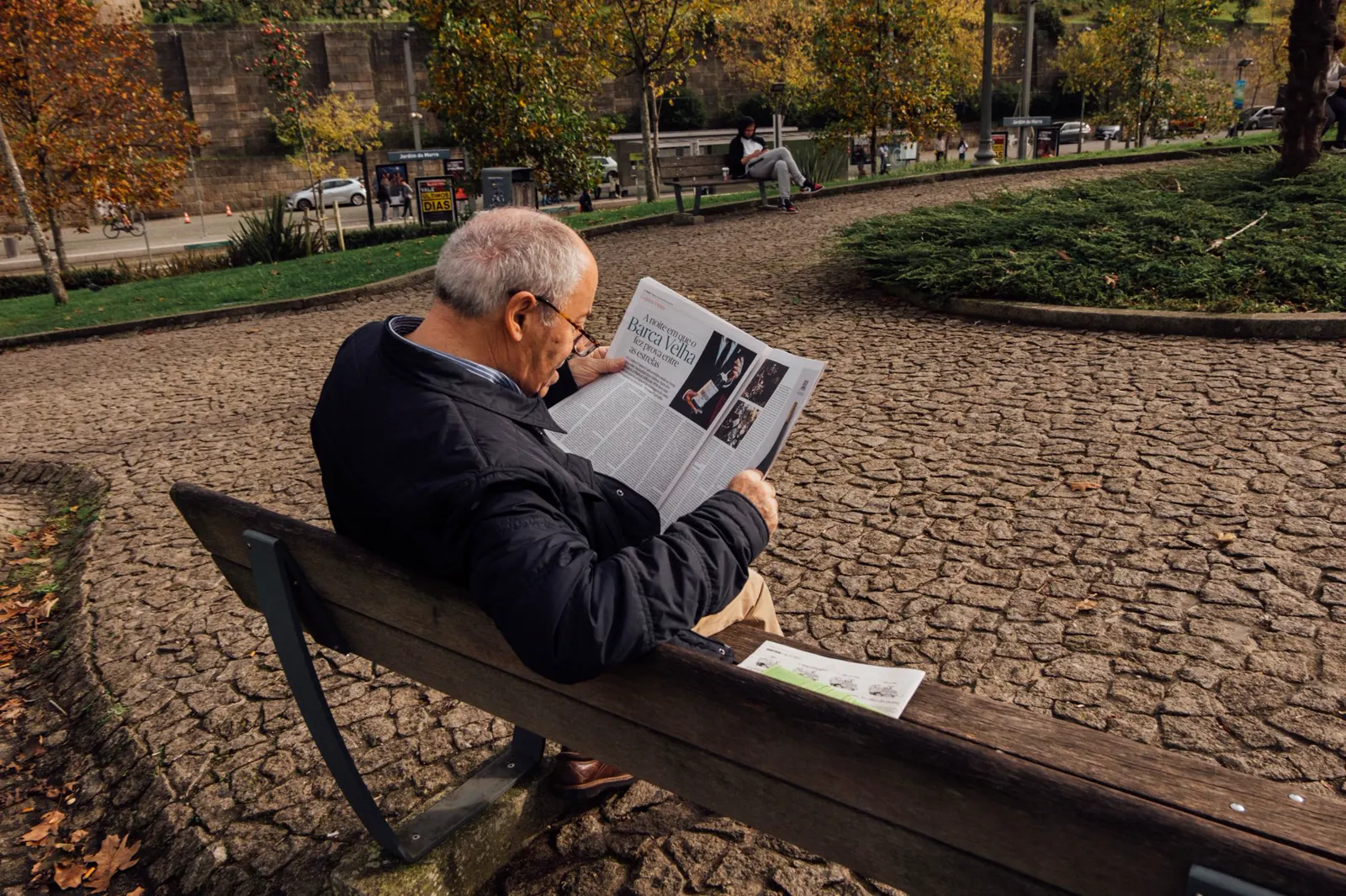 An older man reading on a park bench in autumn