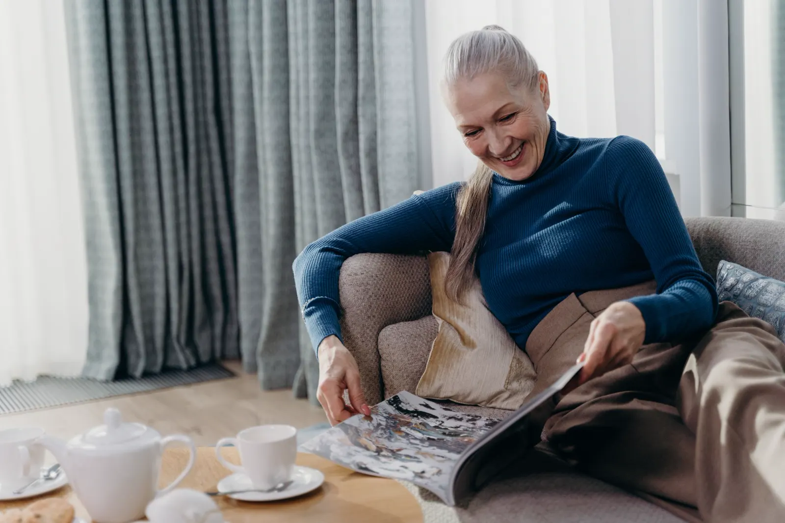 An older woman smiling as she reads a magazine at home