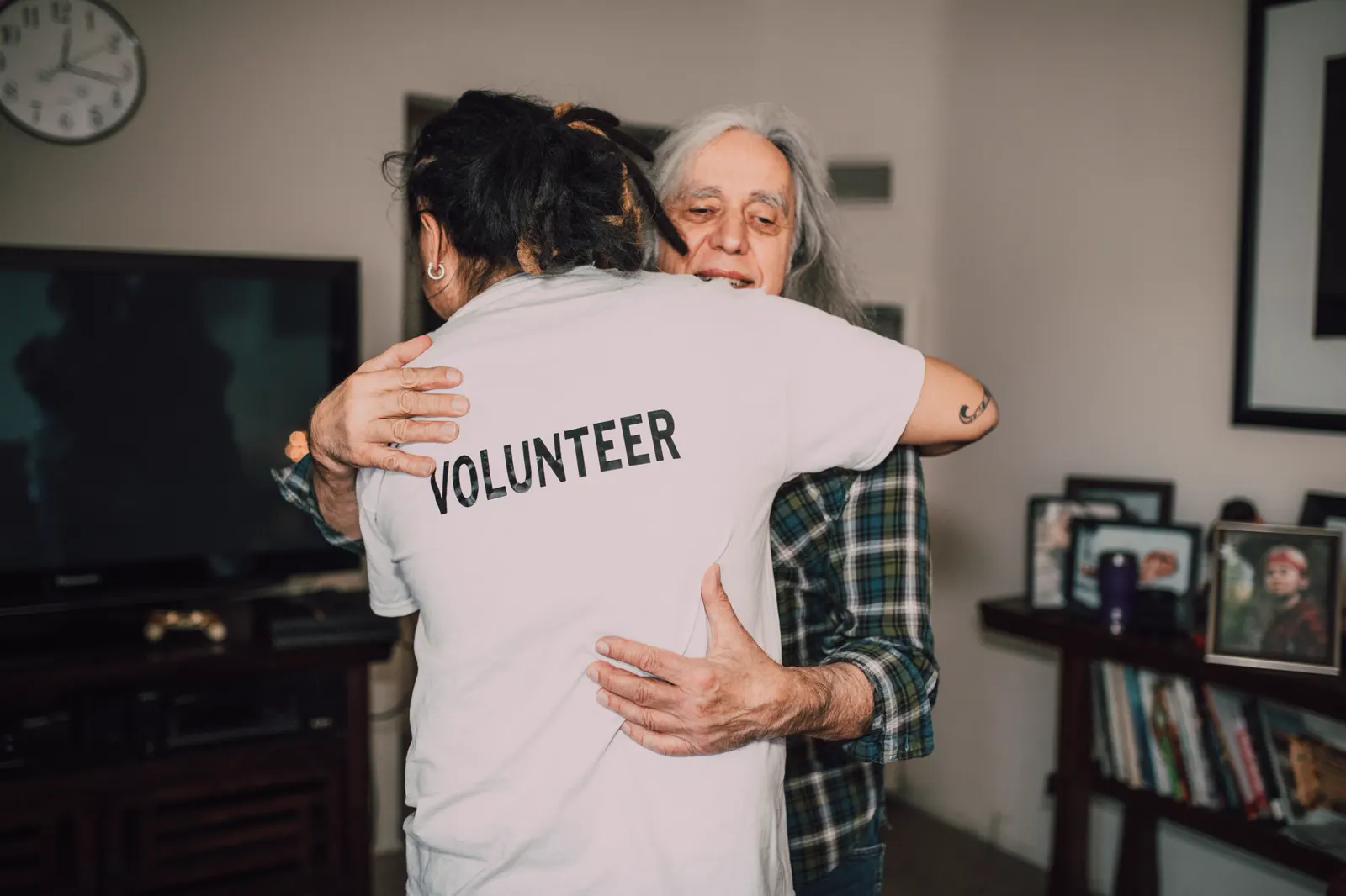 A volunteer embracing an older man in his home
